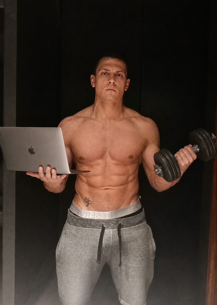 Individual standing with a dumbbell in one hand and a laptop in the other.